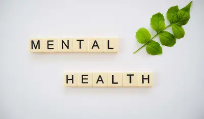 Scrabble tiles spelling the words mental health next to a green leaf