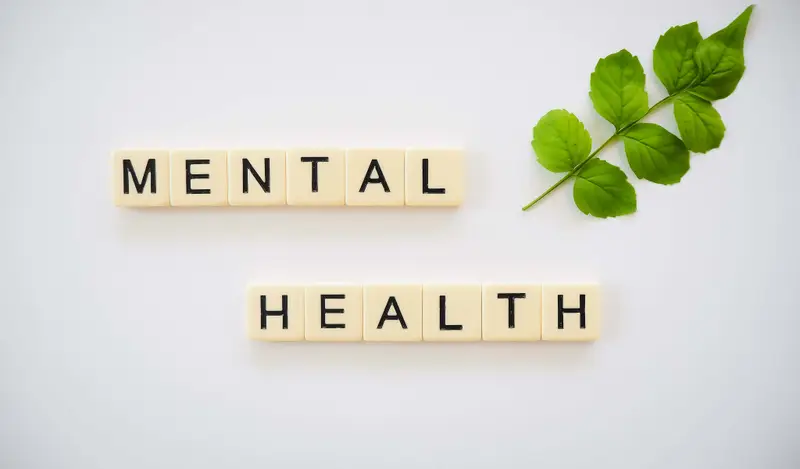 Scrabble tiles spelling the words mental health next to a green leaf