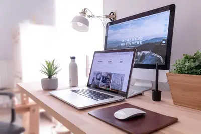 A MacBook Pro on a table beside a white iMac and a Magic Mouse