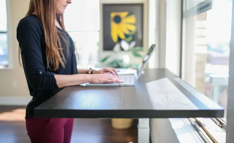 A woman in a black shirt sitting at a table and using a MacBook